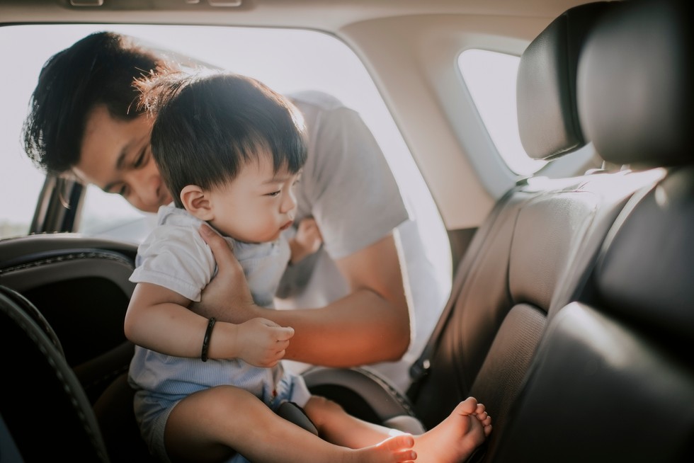 dad putting child into car seat in a car