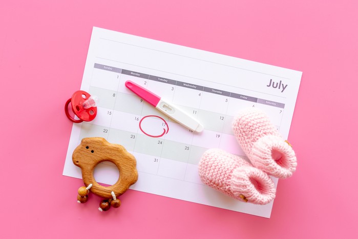 baby bootees and pregnancy test resting on a calendar page showing the baby's due date