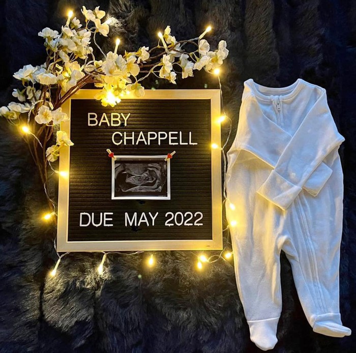 pregnancy announcement using a message board, a sleepsuit, flowers and fairy lights