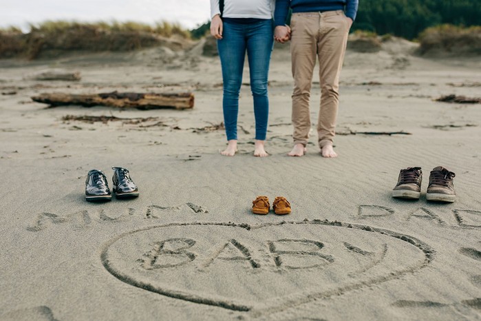 baby written in sand with couple standing behind