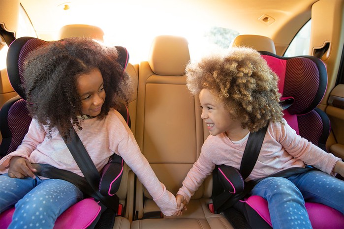 sisters in back of car in car seats, holding hands